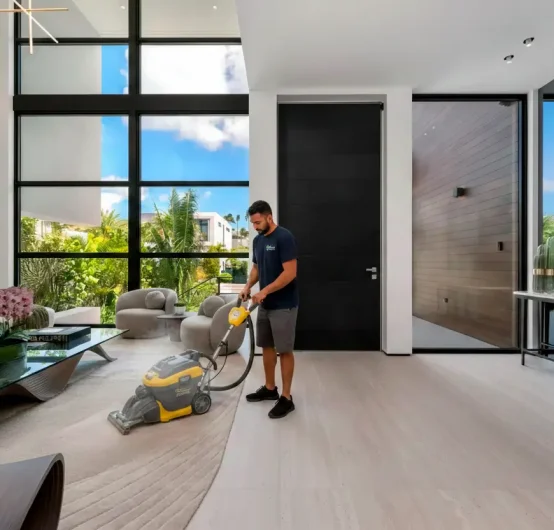 A man uses a carpet cleaning machine for effective surface cleaning on a large, modern living room rug with tall windows, contemporary furniture, and abundant natural light.